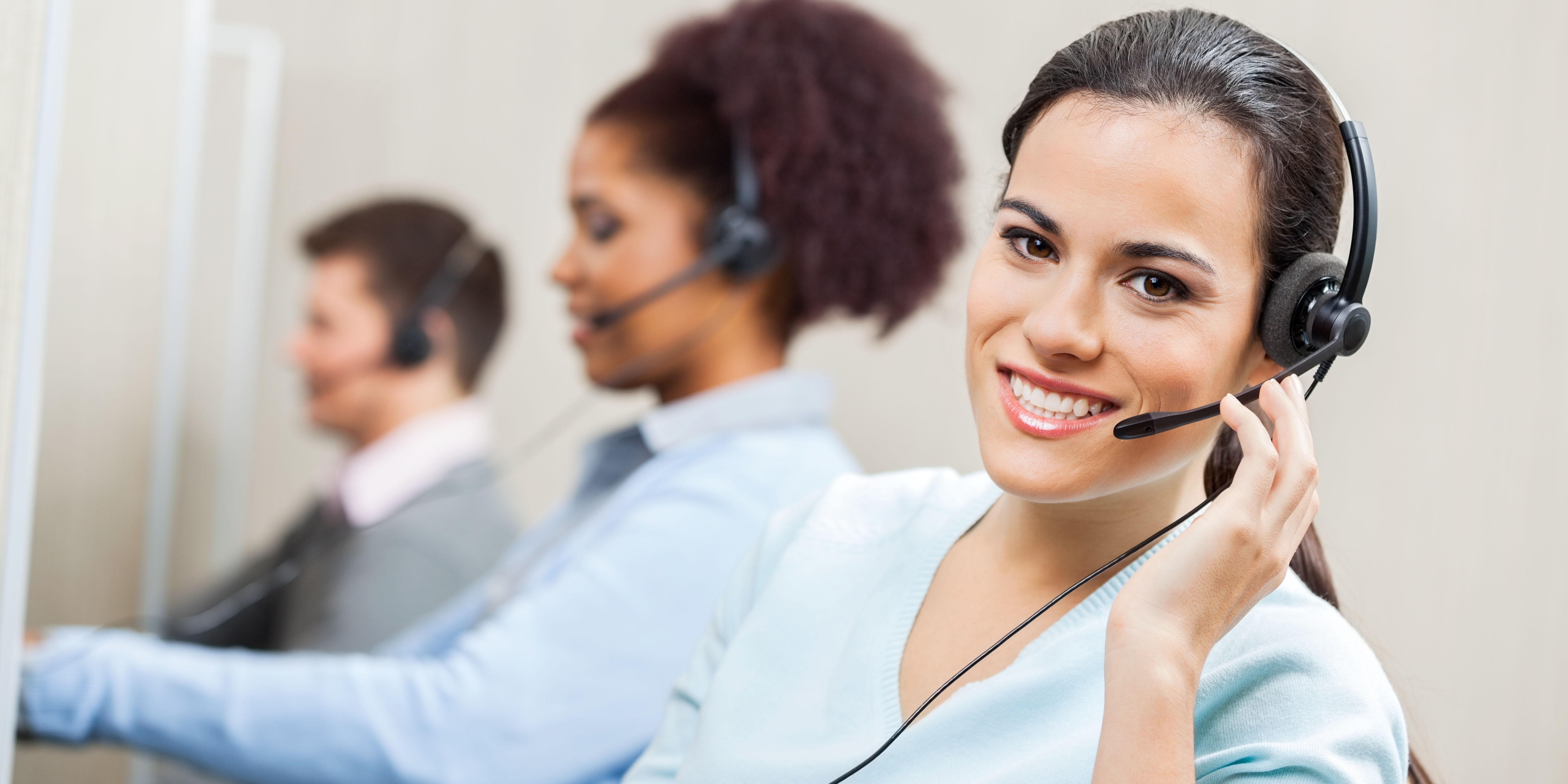 Portrait of smiling female customer service agent wearing headset with colleagues working in background at office